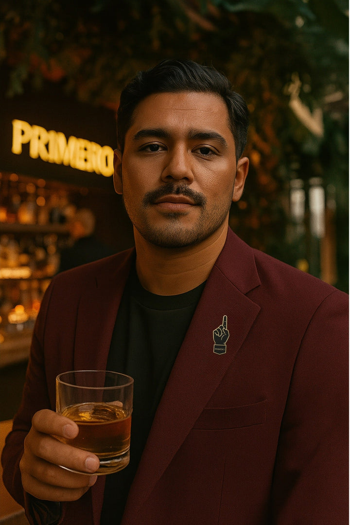Man holding a glass of whiskey in a bar setting with 'Primero' neon sign.