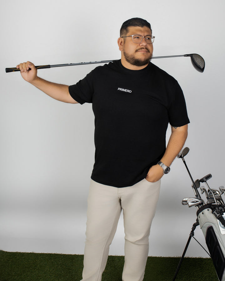 Man holding a golf club with a black shirt and beige pants on a white background