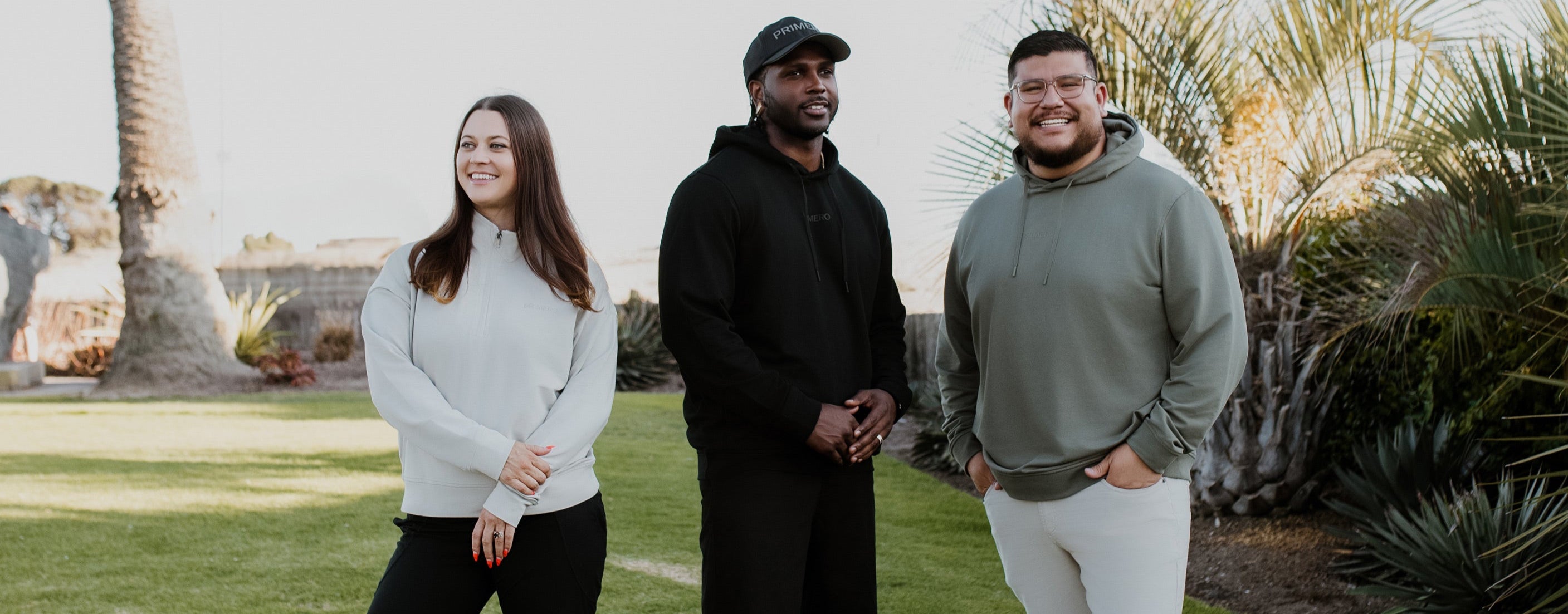 Three people standing on a grassy area with a palm tree and building in the background